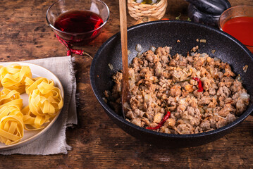 Cooking sausage stew pasta - sausage stew in a frying pan or raw fettuccine nests with ingredients on the table.