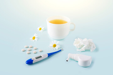 Cup of chamomile tea, thermometer, crumpled paper wipes and spray for runny nose and throat on blue background. Seasonal diseases and treatment of colds, flu, heat. Prevention of virus.