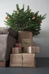 presents in paper wrap with ribbons under christmas tree indoor near couch with natural light