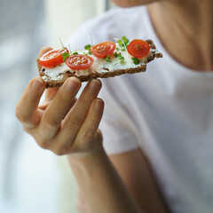 Closeup woman eating rye crisp bread with creamy vegetarian cheese tofu, cherry tomato and rucola...