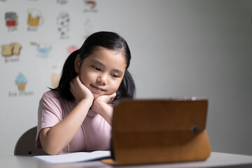 Asian child student learning on computer tablet or kid girl smiling learn from home school or person studying online class and video call education with happy to vocabulary english words in classroom