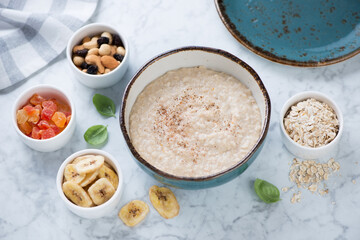 Bowl of oatmeal porridge served with various toppings on a light-grey marble background, studio shot, elevated view