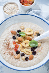 Close-up of oatmeal porridge topped with dried banana slices, candied fruits and nuts, vertical shot