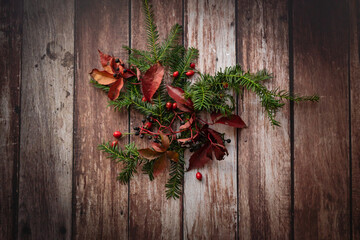 christmas wreath on a brown, old, wooden background with read leaves and rose hips