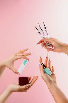 Female hands hold nail polish, brushes and other manicure products on a pink background. Catalog photo. High quality photo