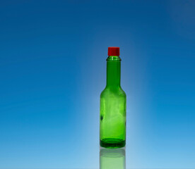Small empty green glass bottle with red cap without label on bright blue background