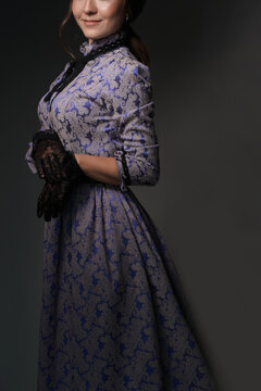 A girl standing in a blue dress in the style of the 1900s, in a retro dress, a hat on a gray background. Historical fashion of the 19th century. High quality photo