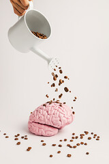 Stream of coffee beans from watering can raining over pink human brain against bright white...