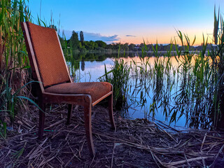 an old chair stands by the lake in the evening