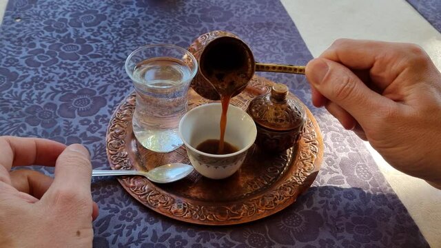 Pouring Turkish coffee from a coffee pot into a cup. Traditional ottoman serving