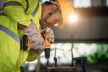 Professional technician in uniform, hat, safety shirt, wear gloves, use electric drill tools to drill workpieces. Safety First in Industrial Factory Concept