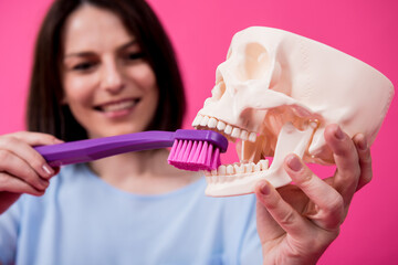 Beautiful woman brushing teeth of an artificial skull using a large toothbrush