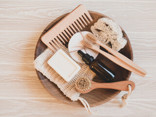 Fototapeta na wymiar Wooden plate,toothbrushes, face brush, comb, aroma oil in amber bottle, soap, cotton pads on wood white table.