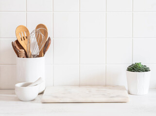 Stylish white kitchen background with kitchen utensils standing on wood countertop near white wall tiles