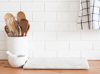 Stylish white kitchen background with kitchen utensils standing on wood countertop near white wall tiles