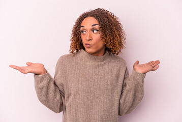 Young latin transsexual woman isolated on pink background confused and doubtful shrugging shoulders to hold a copy space.