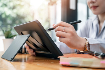Closeup view of woman hand using stylus pen writing on tablet screen while sitting at office desk.
