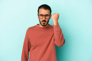 Young caucasian man isolated on blue background showing fist to camera, aggressive facial expression.