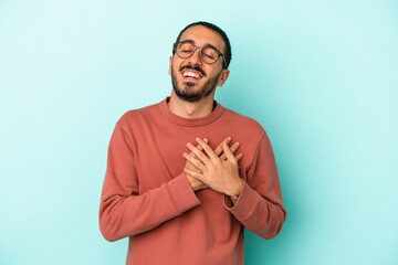 Young caucasian man isolated on blue background laughing keeping hands on heart, concept of happiness.