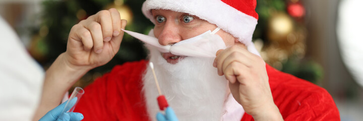 Doctor in rubber gloves taking nasal swab of pcr for santa claus near christmas tree