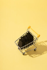 Miniature supermarket cart with shopping bags in black friday sale on yellow background