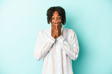 Young african american man isolated on blue background shocked covering mouth with hands.