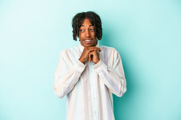 Young african american man isolated on blue background keeps hands under chin, is looking happily aside.