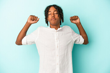 Fototapeta premium Young african american man isolated on blue background stretching arms, relaxed position.