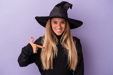 Young Russian woman disguised as a witch celebrating Halloween isolated on purple background person pointing by hand to a shirt copy space, proud and confident