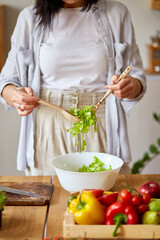 Woman mixing leaf of salad and vegetables ina white bowl