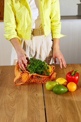 Woman in yellow jacket unpacking shopping mesh eco bag