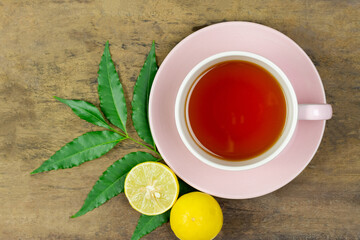 Neem tea in ceramic cup with neem leaf and lemon on wooden background, top view.