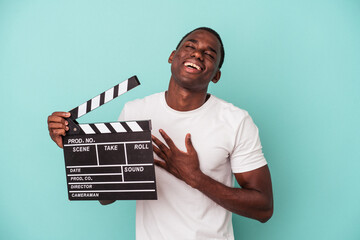 Young African American man holding clapperboard isolated on blue background laughs out loudly...
