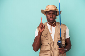 Young African American fisherman holding rod isolated on blue background showing number one with...
