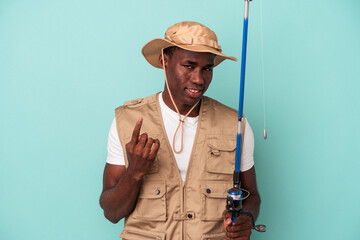 Young African American fisherman holding rod isolated on blue background pointing with finger at you as if inviting come closer.