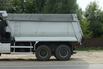 part of a truck with a white large iron body on black wheels stands on the gray asphalt of the road