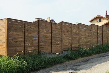 part of a long brown wall of a fence made of wooden planks outdoors in green grass