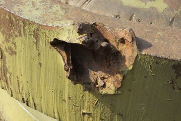 brown rusty hole deformation in a green old iron wall