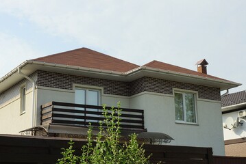 facade of a private gray house with an open brown wooden balcony on the background of the sky outside behind a fence