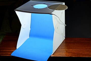 one white square plastic box with lighting for subject photography with blue background on a brown table against a black wall