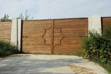 one large closed brown wooden gate and part of the fence wall on the street against the sky