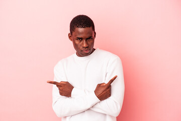 Young African American man isolated on pink background points sideways, is trying to choose between two options.