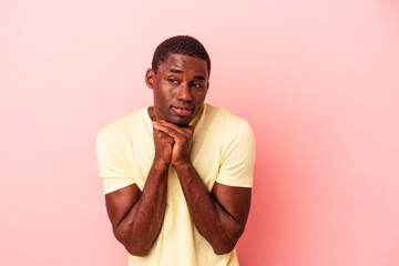 Young African American man isolated on pink background keeps hands under chin, is looking happily aside.