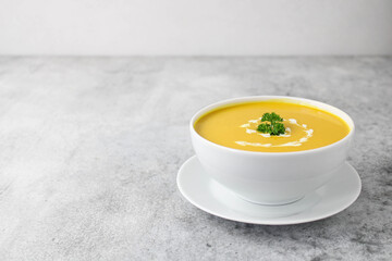 Pumpkin and carrot soup with cream, parsley and seeds on a gray background, copy space