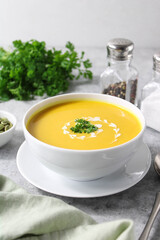 Pumpkin and carrot soup with coconut cream, parsley and seeds on a light background