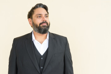 Portrait of handsome bearded Indian businessman against plain background