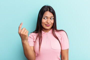 Young Venezuelan woman isolated on blue background pointing with finger at you as if inviting come closer.