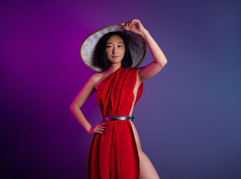 asian woman in red cape and asian hat posing on bright neon background