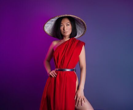 asian woman in red cape and asian hat posing on bright neon background
