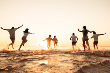 Big group of young friends or big family are having fun and run at sunset beach. Summer vacations...